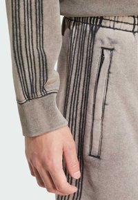 Gray cotton sweatshirt featuring long sleeves with ribbed cuffs and vertical black stitching detail. Includes a zippered pocket on the side.