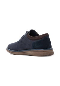 Zapatos de cuero azul marino con un acento de tacón de ante y suela de goma texturizada, presentando una punta redondeada y diseño de cordones.
