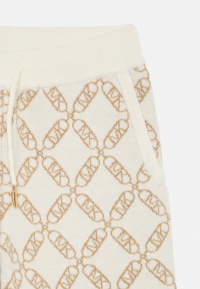 Pantalons de survêtement crème avec un motif de logo répétitif couleur marron clair sur toute la surface, accentués par un cordon de serrage et des poches latérales.