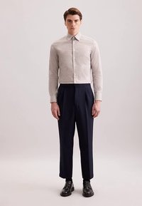 Geruit overhemd met knopen in lichtbeige en donkerbruin, gecombineerd met op maat gemaakte marineblauwe broek en zwarte leren schoenen.