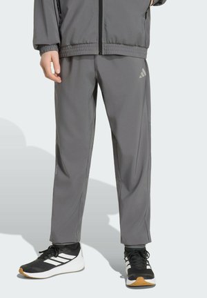 Persona con pantalones deportivos grises y chaqueta a juego, combinados con zapatillas Adidas negras y blancas con suelas de goma.