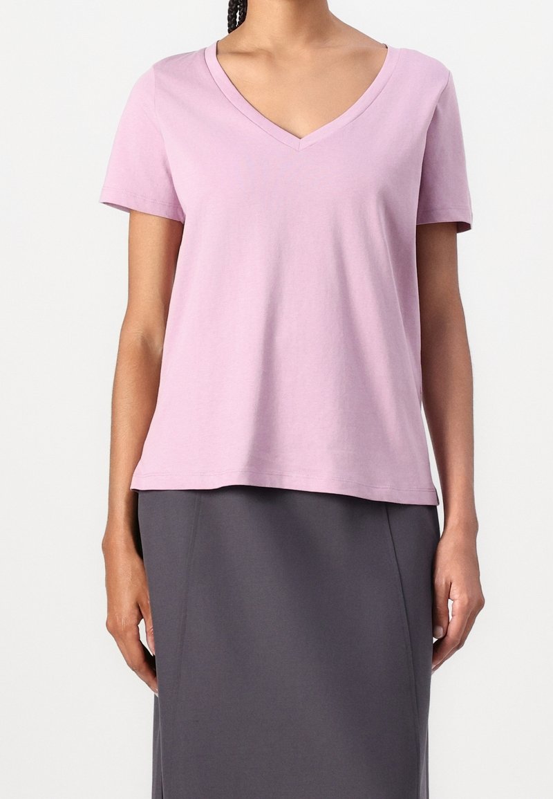 Rosa bomullströja med v-ringning och korta ärmar, ihop med en grå kjol. Tyget verkar mjukt och lätt. Enkelt design.