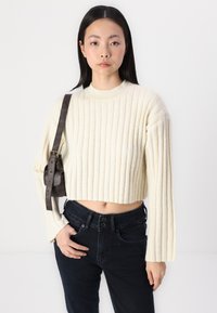Kremfarget ribbestrikket genser med lange ermer og cropped lengde, kombinert med mørke denimjeans. Genseren har rund hals og strukturert stoff.