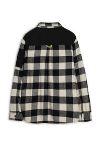 Camisa de cuadros en negro y crema, con una pechera negra sólida en contraste, puños abotonados y un detalle de pliegue en la parte trasera.