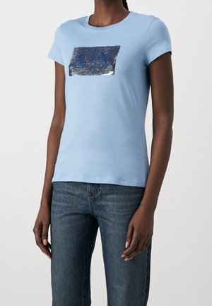 Hellblaues T-Shirt aus Baumwolle mit kurzen Ärmeln. Vorderseitig mit einem rechteckigen Pailletten-Design in Blau und Silber versehen. Klassische Passform.