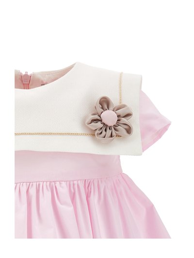 Vestitino rosa per bambina con maniche a sbuffo, colletto crema con texture, bordatura dorata e decorazione floreale beige in tessuto sul petto.