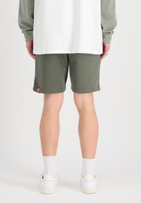 Shorts vert olive avec une coupe décontractée, dotés d'une taille plate et de coutures latérales. Des chaussettes blanches et des baskets blanches complètent le look.
