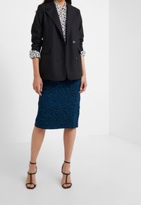 Black double-breasted blazer over a white shirt with black spots, paired with a blue leopard print pencil skirt and black strappy heels.