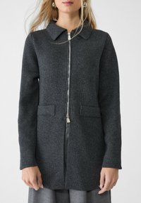Dunkelgrauer Strickmantel mit kragenförmigem Hals, vollem Frontreißverschluss und zwei vorderen Taschen. Lange Ärmel und ein strukturiertes Material.