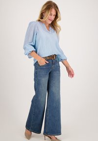 Lichtblauw, geribbeld blouse met een V-hals en pof halve mouwen, gecombineerd met brede donkere spijkerbroeken en beige hakken. Eenvoudige bruine riem.