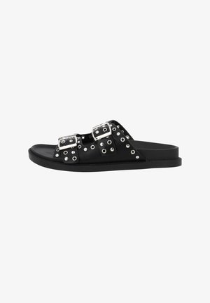 Sandalo nero slip-on con due cinturini regolabili con fibbie decorati con borchie e occhielli argentati, suola piatta, vista laterale.