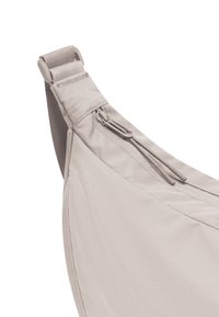 Világosszürke anyagú sling táska sima textúrával, cipzáras zsebbel és állítható pánttal, minimális dizájn jellemzi.