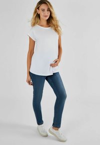 T-shirt bianca a maniche corte con scollatura rotonda, abbinata a jeans attillati blu scuro e sneakers bianche. Design semplice e casual.