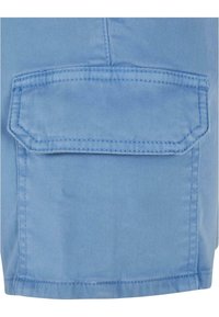 Gros plan d'une poche cargo en tissu bleu avec rabat et coutures visibles sur un vêtement, probablement un short ou un pantalon.