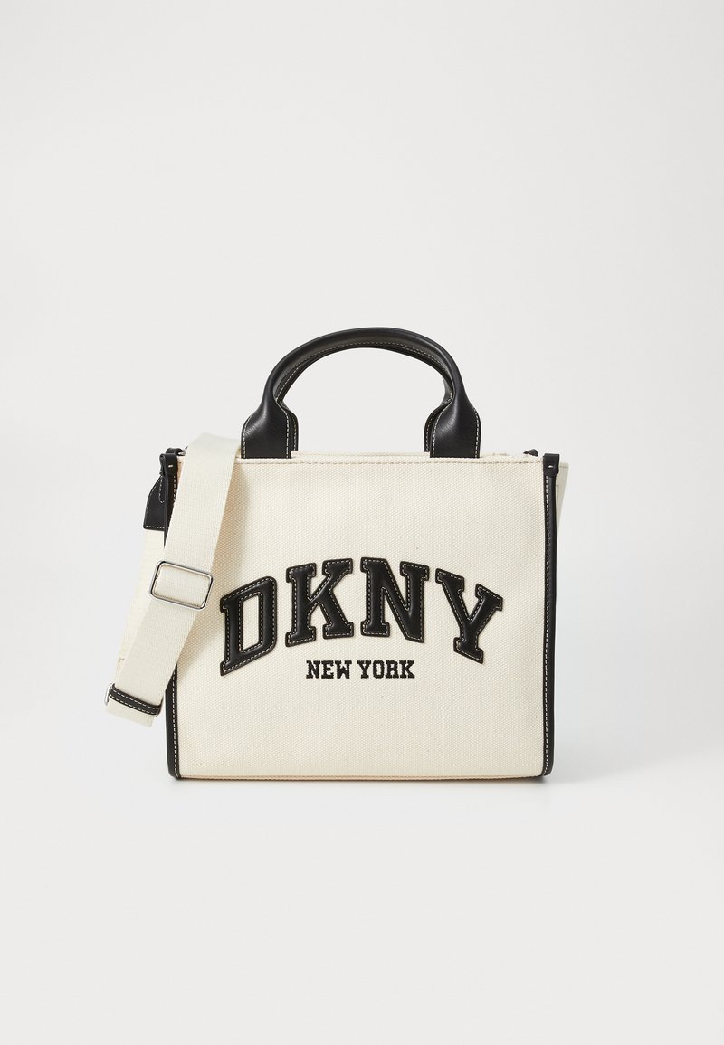 Kreminė kanvos rankinė su juodais odiniais akcentais. Pasižymi viršutine rankena ir nuimama juosta. Išsiuvinėtas „DKNY NEW YORK“ logotipas išsiskiria.