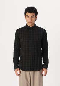 Camisa negra de manga larga con un patrón de rayas verticales, con cuello abotonado, botones en la parte frontal y un corte relajado. Textura de tela suave.