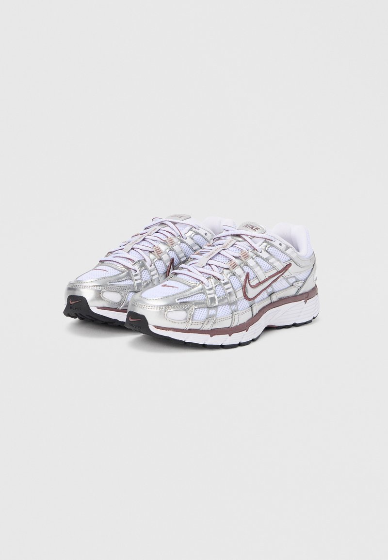 Chaussures de sport argentées et blanches avec une tige en mesh, des accents réfléchissants et une semelle coussinée. Détail avec un logo Nike bordeaux.