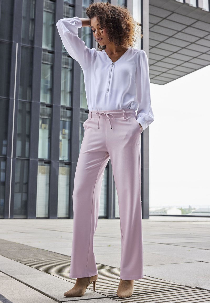 Svetloružové nohavice so rovnými nohavicami a pásom na šnúrku, skombinované s bielou blúzkou s dlhým rukávom a zipsom.