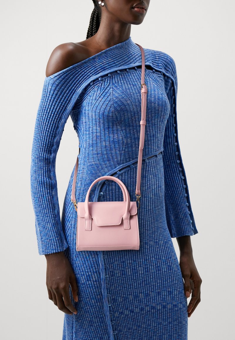 Nainen, jolla on yllään sininen ribbattu olkaimeton mekko, jossa on napitusyksityiskohtia, sekä pieni vaaleanpunainen käsilaukku yläkahvalla ja olkahihnalla.