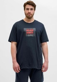 Mørkeblå bomulds T-shirt med et kvadratisk grafik, hvor "JACK & JONES" står med fed rød tekst. Løs pasform med korte ærmer og rund hals.