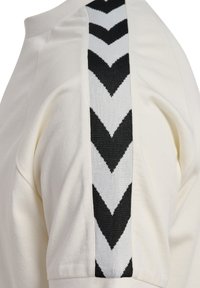 Haut blanc à manches courtes avec un motif en chevrons noir et blanc sur le côté. Tissu doux avec une coupe décontractée.