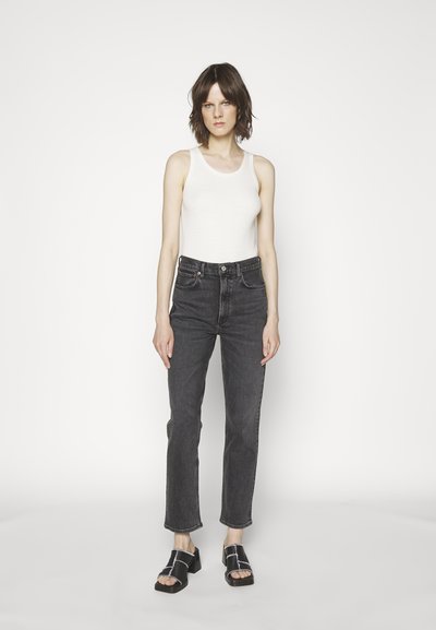 Balta dryžuota marškinėlių su aukštu juosmeniu tamsiai pilki džinsai su tiesiomis kojomis ir juodi platforminiai sandalai su sidabro detalėmis.