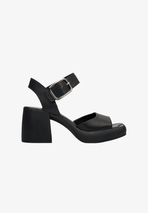 Sandales à talons en cuir noir avec un bout ouvert arrondi, une sangle de cheville ajustable et un talon épais. Texture lisse avec une finition brillante.