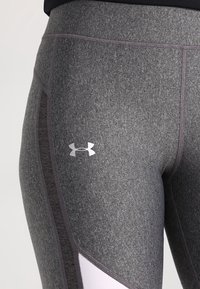 Lähikuva harmaista urheilulegginsseistä, joissa on tummat sivupaneelit ja valkoinen Under Armour -logo yläreidessä.