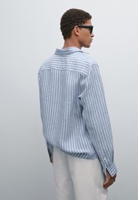 Blue and white striped shirt with long sleeves, button cuffs, and a spread collar. Made of lightweight fabric, relaxed fit with a curved hem.