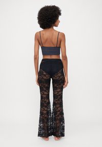 Pantaloni svasati in pizzo nero con motivo floreale, indossati con un top corto grigio scuro con spalline sottili, che mette in risalto una schiena liscia.