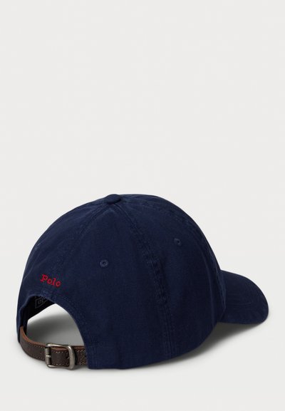 Marineblå baseballcaps med justerbar brun læderrem og rød "Polo" broderi på bagsiden, præsenteret på en hvid baggrund.