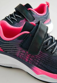Baskets de sport bleu foncé avec des accents roses et un design texturé. Les caractéristiques incluent une sangle Velcro, un tissu en mailles et une semelle blanche.