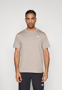 Μπεζ κοντομάνικη μπλούζα με στρογγυλή λαιμόκοψη από απαλό βαμβάκι· διαθέτει μικρό λευκό λογότυπο στο πάνω αριστερό μέρος του στήθους.