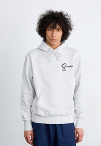Light gray hoodie with a kangaroo pocket, drawstring hood, and a printed logo on the chest. Fabric appears soft and textured.