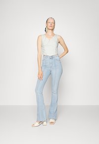 Top cinza claro cropped com decote em V, combinado com jeans azuis claros e flare. Modelo usa sandálias de bloco de salto em creme; design simples e limpo.
