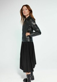 Czarna skórzana kurtka z zamkami błyskawicznymi, dopasowany krój, żebrowane ramiona, w połączeniu z czarną plisowaną spódnicą i masywnymi czarnymi botkami.