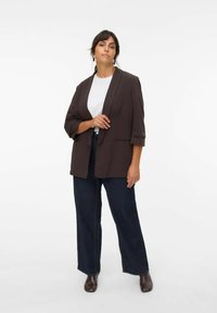 Hnědý blazer s tříčtvrtečními rukávy, kombinovaný s bílým tričkem a tmavými širokými džíny. Hladká látka, minimalistický design, bez vzorů.