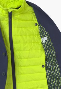 Marineblaue Außenjacke mit einem leuchtend grünen, gesteppten Futter; verfügt über einen durchgehenden Reißverschluss, einen Druckknopfverschluss und ein gemustertes Innenfutter.