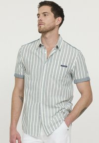 Chemise à manches courtes en beige clair et rayures grises. Comprend une poche poitrine, des manches retroussées, et une étiquette indiquant "Lee Cooper".