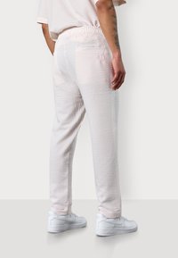 Weiße Jogginghosen mit Struktur und elastischem Bund, die ein dezentes Karomuster und einen rosa Akzent auf der Gesäßtasche bieten.