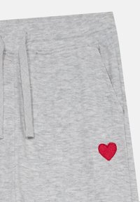 Pantaloni in maglia grigi chiari con tasche laterali, vita con cordoncino e un piccolo cuore ricamato rosso vicino alla tasca.