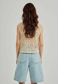 Kanten haaktop in lichtbeige met bloemen hexagonpatronen, gecombineerd met hooggerode lichte denim shorts.