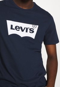 T-shirt in cotone blu navy con il logo bianco di Levi's in un design curvato sul petto. Maniche corte e scollatura a girocollo.