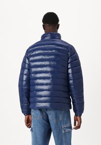 Mørkeblå dunjakke med blank, quiltet overflade, høj krave og ribbet kant. Bæres med lyseblå cargobukser.