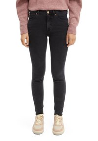Vaqueros skinny negros de cintura alta, con cinco bolsillos y herrajes dorados. Combinados con zapatillas de color claro y un suéter rosa.