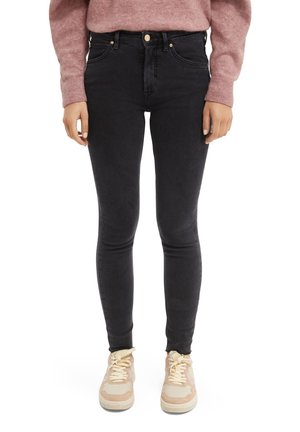 Vaqueros skinny negros de cintura alta, con cinco bolsillos y herrajes dorados. Combinados con zapatillas de color claro y un suéter rosa.