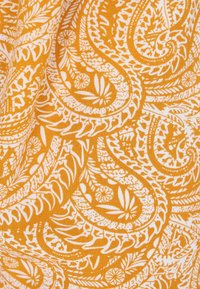 Geel textiel met complexe witte paisleypatronen, versierd met bloem- en loofmotieven, met een gestructureerd oppervlak en symmetrische designelementen.