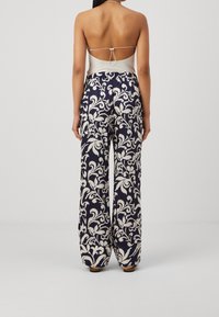 Bakvy av en person som bär en vit, åtsittande topp med låg rygg och marinblå vida byxor med ett vitt blommönster.