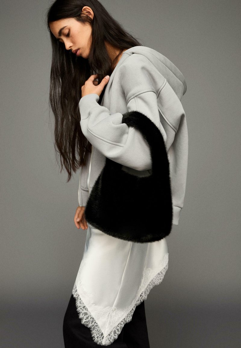 Fekete műszőrme válltáska szürke kapucnis pulóver mellett, fehér szatén szoknyával, amely csipke szegéllyel díszített, valamint fekete nadrággal.