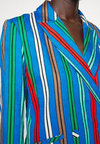 Meer kleurige blazer met opvallende verticale strepen in blauw, groen, bruin, rood en wit, voorzien van een gestructureerde reverskraag en knoopdetail.